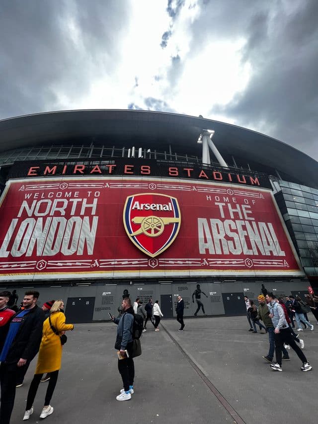 Emirates Stadium exterior Welcome to North London and Home of The Arsenal banner with club crest fans walking outside matchday