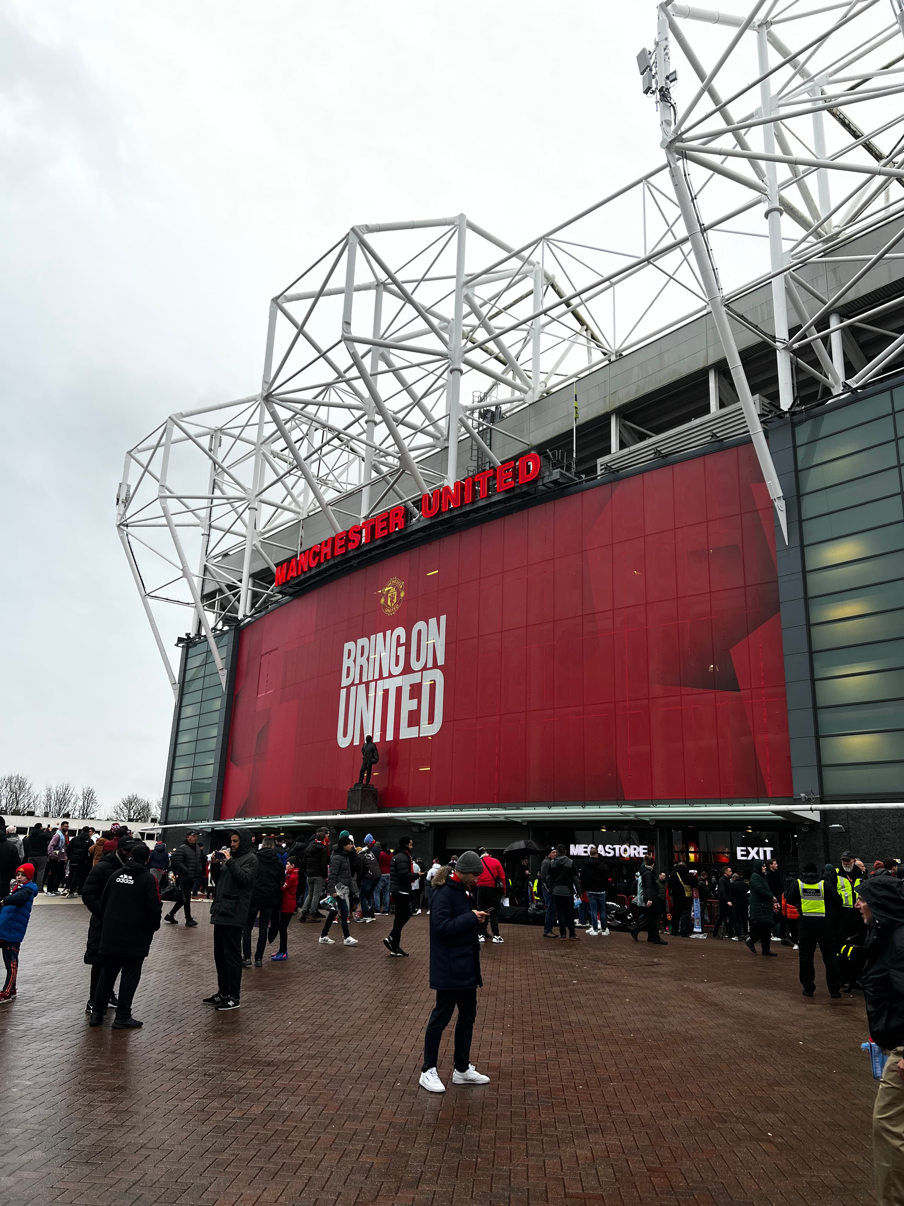 Old Trafford stadium exterior Manchester United Megastore entrance Bring On United banner fans gathering matchday Theatre of Dreams